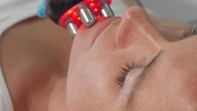Sliding cropped shot of a mature woman getting facial rf-lifting procedure. Female client receiving facial anti-age treatment by cosmetologist. Beauty, dermatology concept