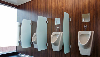 Weiße Urinale an Holzwand in Herrentoilette auf Kreuzfahrtschiff - Ceramic urinals in row with...