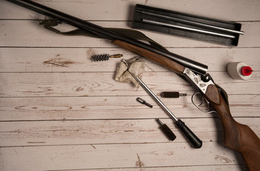 Hunting equipment. Hunting rifle, barrel cleaning equipment, ramrod, ruff, oil on a light wooden background.
