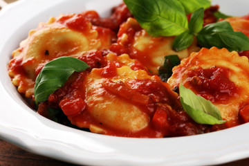 Ravioli with tomato sauce garnished with parmesan cheese and basil on rustic table