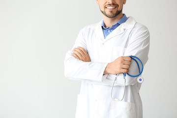 Male doctor with stethoscope on light background