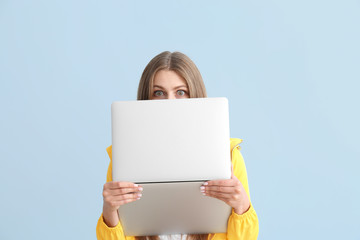 Surprised young woman with laptop on color background