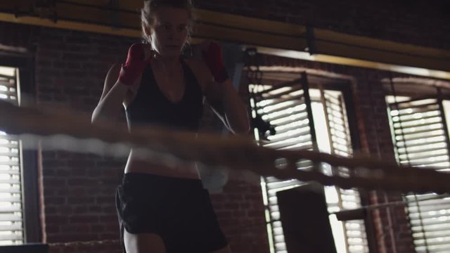 Caucasian young female MMA fighter wearing racerback tank top and shorts practicing inside boxing ring