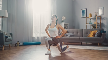 Strong and Beautiful Athletic Fitness Girl in Sportswear is Doing Forward Lunge Exercises in Her Bright and Spacious Living Room with Minimalistic Interior.