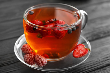 Glass cup of tasty tea with berries on dark wooden table, closeup