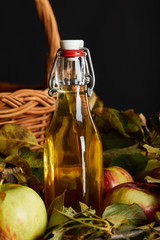 bottle of cider near wicker basket and apples on wooden surface