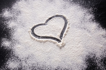 A heart shape drawn on flour on a black background. Close-up.