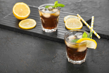 Glasses of cold cola and lemon on dark table