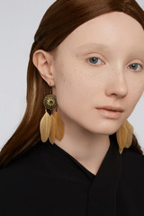 Cropped portrait shot of a young stylish European girl with bronze hook earrings made in the form...