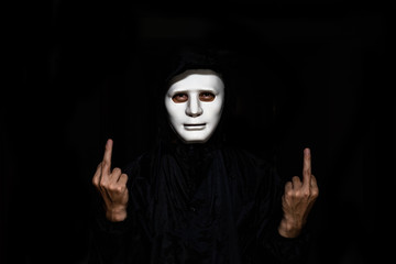 unrecognizable young man white mask and hoodie showing Middle Finger at Camera isolated on black Background.