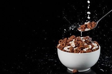 white bowl with assorted cereal and spoon with milk drops isolated on black
