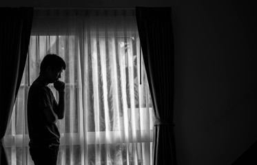 Alone man silhouette standing at the window closed with curtains in bedroom. Man stands at window alone, Depression and anxiety disorder concept.