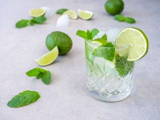 A mojito cocktail made from fresh mint and lime in a cut glass tumbler against a pale background
