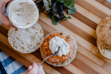 A woman hand putting homemade tartar sauce over a salmon and prawns hamburger. Vegetarian Food