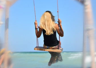 Back view of happy blonde hair girl on swing ,on the shore of the sea. Creative image.