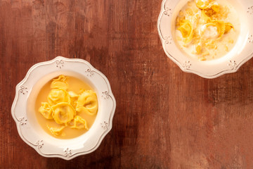 Tortellini served with broth and cream sauce, Italian food on a dark rustic wooden background with a place for text