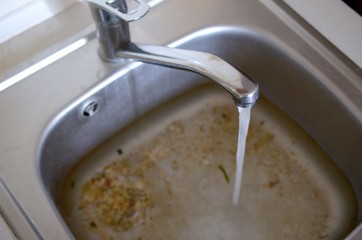 Stainless steel sink plug hole close up full of water and particles of food