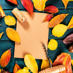 Autumn wine design template with a wine cork and corkscrew on a brown kraft paper with vibrant fall leaves forming a frame for text and logo, on a dark rustic wooden background