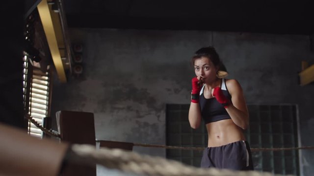 Tilt up of Caucasian young female kickboxer wearing sport clothes and red wrist bands training shadow boxing in boxing ring