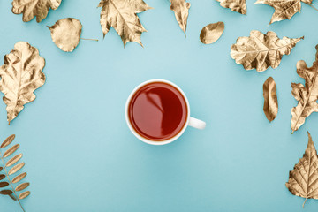 top view of warm tea in mug near golden foliage on blue background