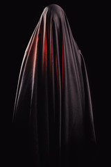 woman covered with black cloth stands on an isolated black background. faceless death concept