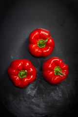 Fresh three red peppers on a black background in the center of the frame. View from above.