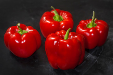 Fresh four red peppers on a black background in the center of the frame.