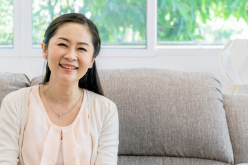 Middle aged Asian woman portrait sitting on a couch indoors.