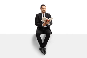 Businessman sitting on a banner with a book and looking at the camera