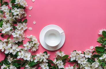 An empty cup of tea stands on a pink background surrounded by white flowers of an apple tree. The concept of spring tea and medicinal decoctions. Copy space.