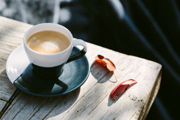 A cup of coffee on a wooden table outdoors on a sunny day