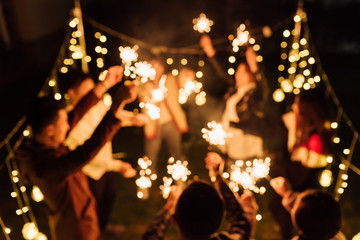 Group of friends holding burning sparklers and dancing