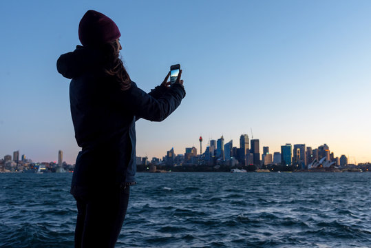 Woman photographing Sydney skyline at sunset
