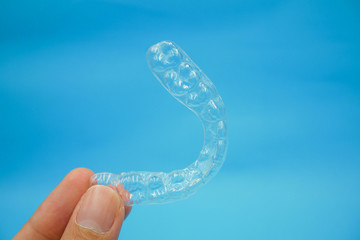 hand holding clear plastic retainer teeth that isolated on blue sky background. it's an equipment for orthodontist give the patient to orthodontic surgery in dental clinic or hospital