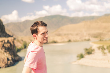 Fototapeta na wymiar young smiling man in a pink t-shirt on a background of mountains on a sunny summer day