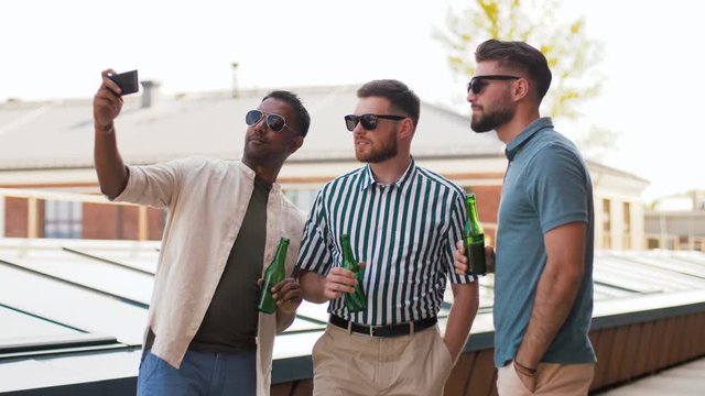 leisure, technology and people concept - happy male friends taking selfie by smartphone and drinking beer at rooftop party in summer