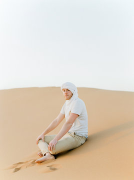 A European man in a desert wearing white beduin hat