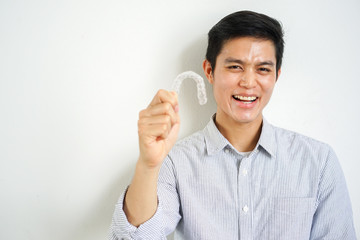 close up young asian man smiling with hand holding dental aligner retainer (invisible) at dental clinic for beautiful teeth treatment course concept	