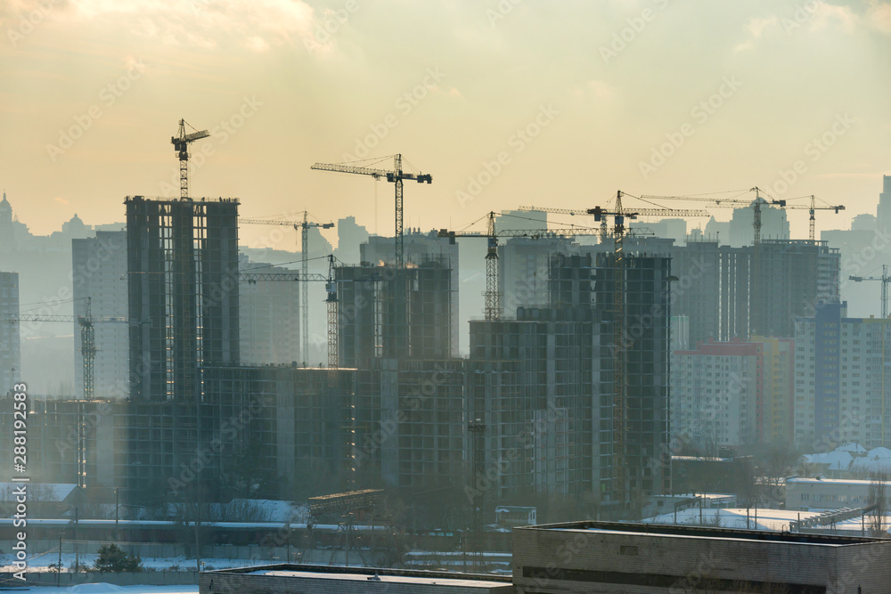 Wall mural Constraction site with industrial cranes in city at sunset