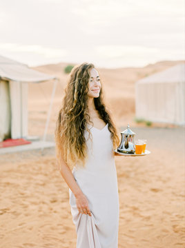 A portrait of a dark-haired woman serving moroccan mint tea in the desert camp
