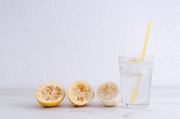 Glass of water with lemon and squeezed lemons on a wooden table.