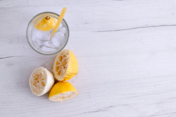 Glass of water with lemon and squeezed lemons on a wooden table.