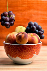 Seasonal fruits, grapes, mango, apple, peach, placed on a plastic bold sibre a wooden table and a diffuse background with hanging grapes and orange wood