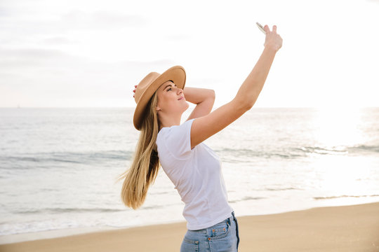 Blonde girl wearing hat holding cell phone taking a picture of herself