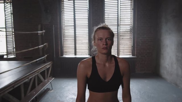 Medium shot of young Caucasian woman wearing black racerback tank top and shorts standing in gym and looking at camera