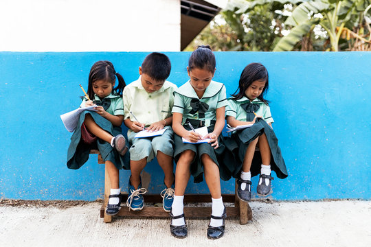 Asian schoolkids doing homework on bench