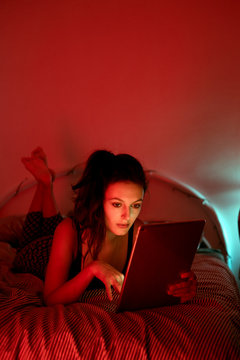 Attractive young girl in lingerie lying on the bed and using the tablet