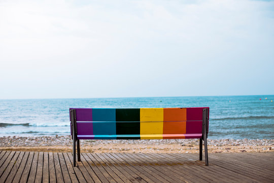 Rainbow colored bench in front of sea