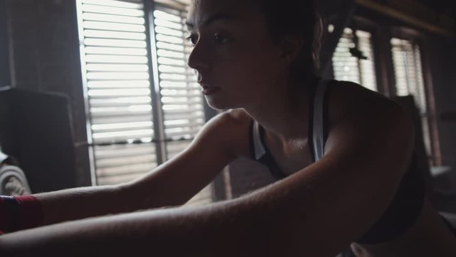 Close up of young female boxer standing inside boxing ring, leaning on rope and catching breath