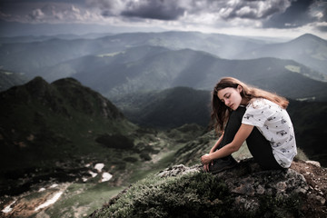 Naklejka na ściany i meble Young woman sitting on a mountain top. Woman hiking around mountains. Calm and inspiration on high peak of mountain